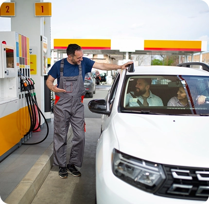 Posto de combustível, com um frentista atendendo duas pessoas que estão dentro de um carro branco.