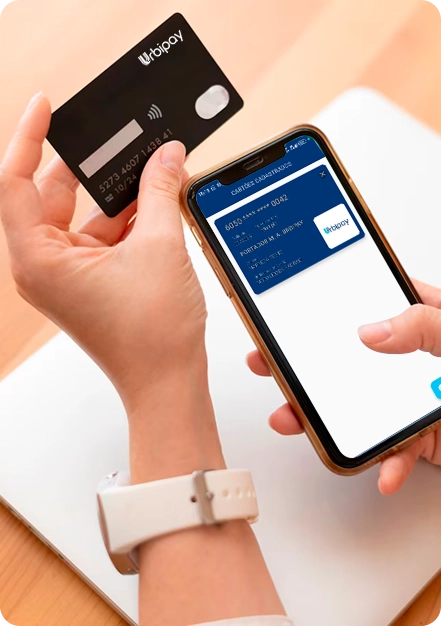 Mãos femininas segurando um smartphone e um cartão alimentação Urbipay